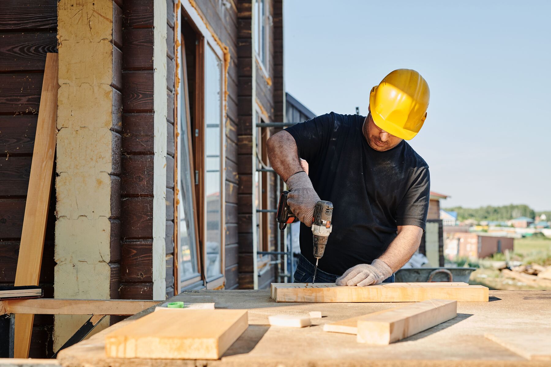 Contractor in a hard hat drilling a board outside a home